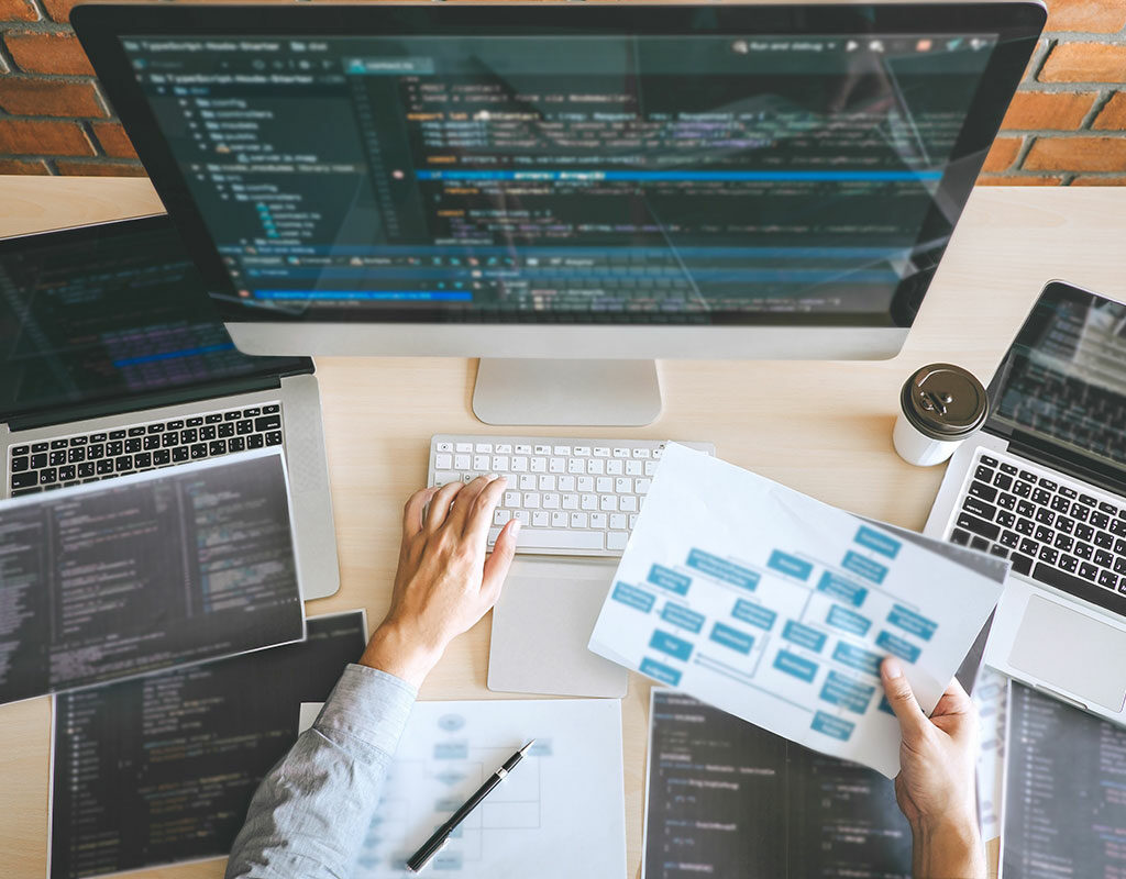 Person working on a Website with 3 computers and a sitemap in their hand