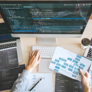 Person working on a Website with 3 computers and a sitemap in their hand