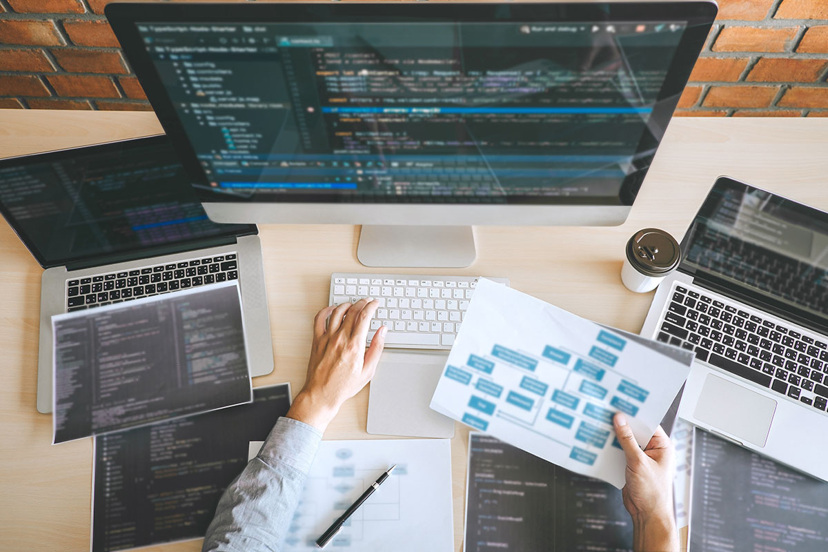 Person working on a Website with 3 computers and a sitemap in their hand
