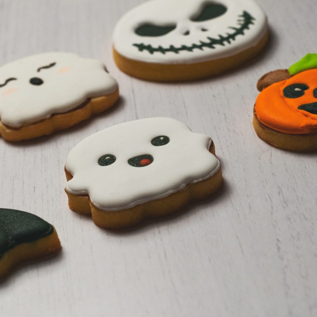 A selection of Halloween-themed decorated cookies in the shapes of ghosts and pumpkin on a light wooden surface.