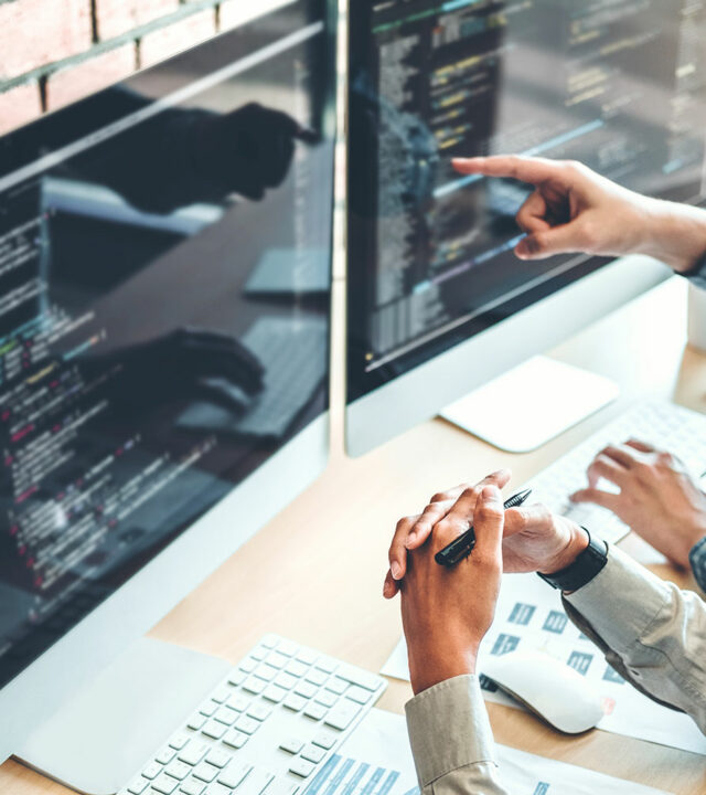 Two people sitting at a workstation looking at web code